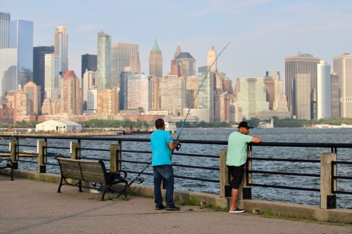 Two fishermen fish in the Hudson River from the pier in front of Manhattan Skyline 