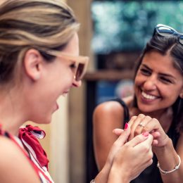 Two beautiful happy female friends in cafe showing engagement ring