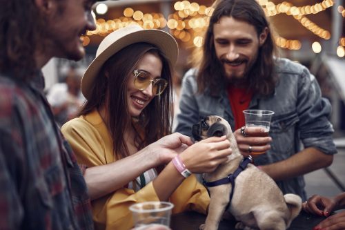 Portrait of stylish hipster friends looking at cute dog and smiling.