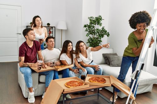 Group of young friends eating pizza and playing Pictionary at home.