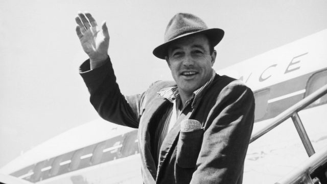 Gene Kelly waving from the steps of a plane circa 1950s