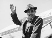 Gene Kelly waving from the steps of a plane circa 1950s