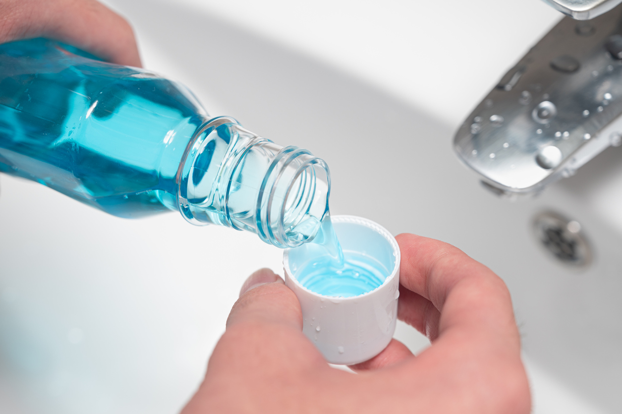 Hand pouring bottle of mouthwash into cap.