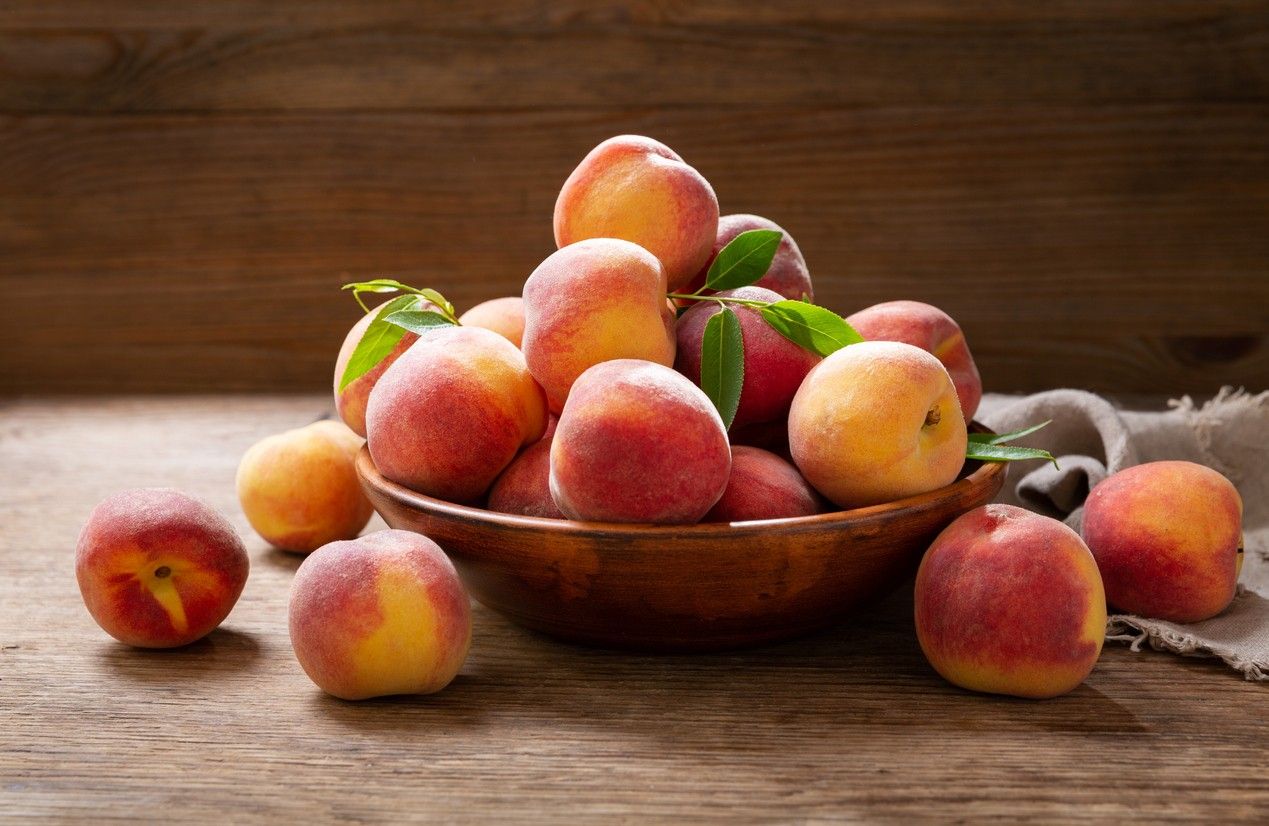 bowl of fresh ripe peaches on a wooden background