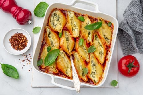 Ricotta and spinach stuffed shell pasta with tomato sauce in white baking dish, white background