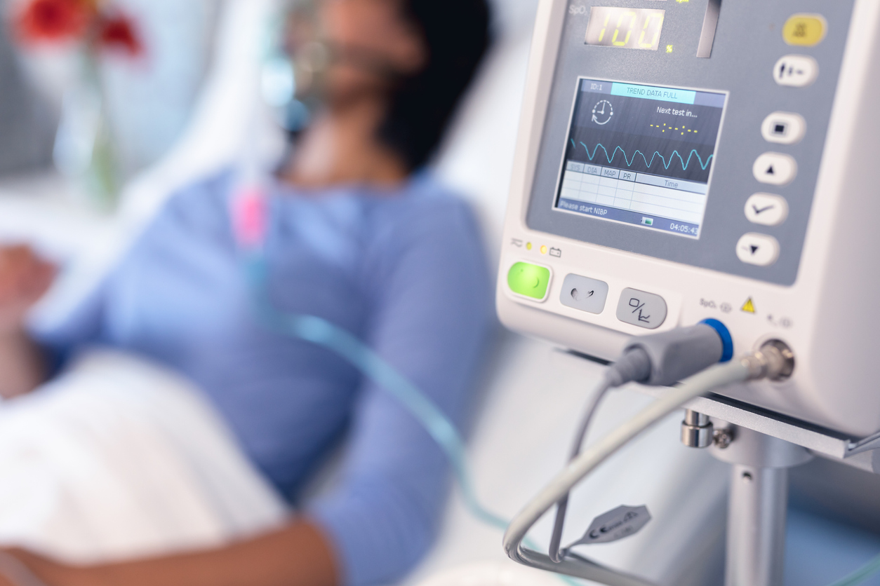 Ventilator monitor and patient in hospital bed with oxygen ventilator.