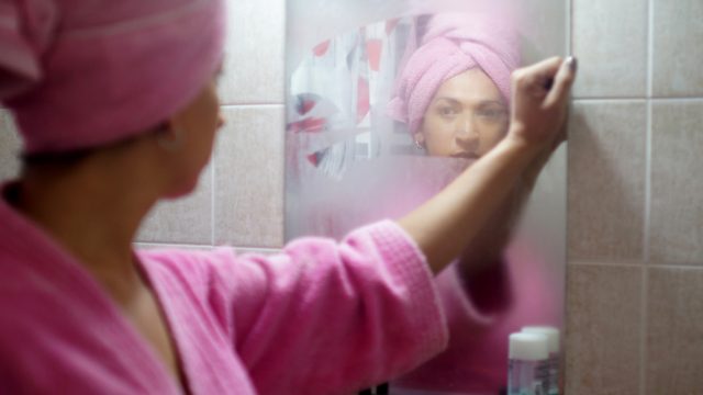 Woman looking at herself in bathroom mirror.