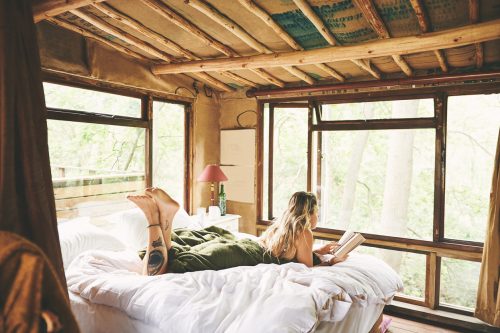 Shot of a young woman reading a book while lying on a bed in a cabin
