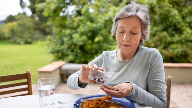 Woman taking medication with food at a table.