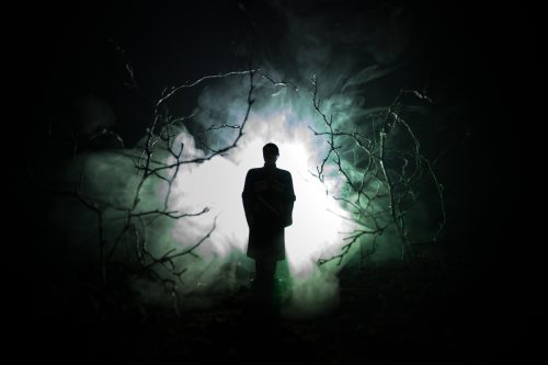 eerie silhouette in dark spooky forest at night, surreal lights of mystical landscape with creepy man