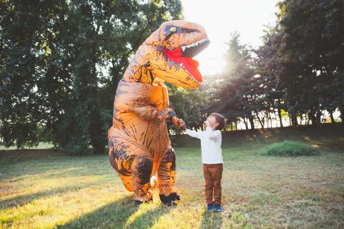 Father and son playing in the park with the dad dressed up in an inflatable dinosaur costume
