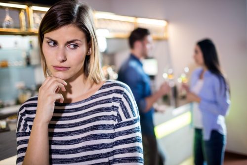 Upset woman with hand on chin while boyfriend talking with female friend in background.
