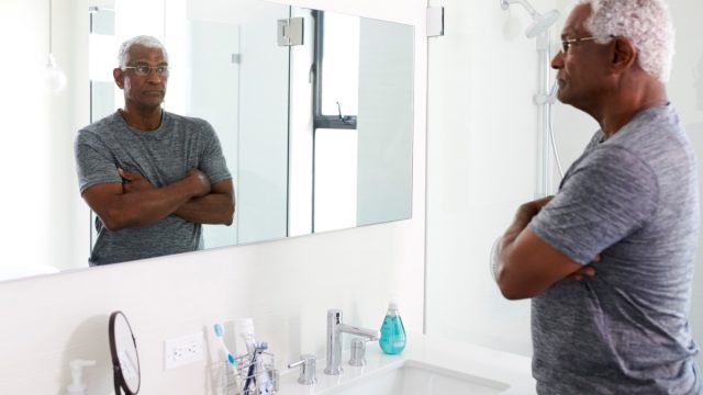 Unhappy Depressed Senior Man Looking At Reflection In Bathroom Mirror