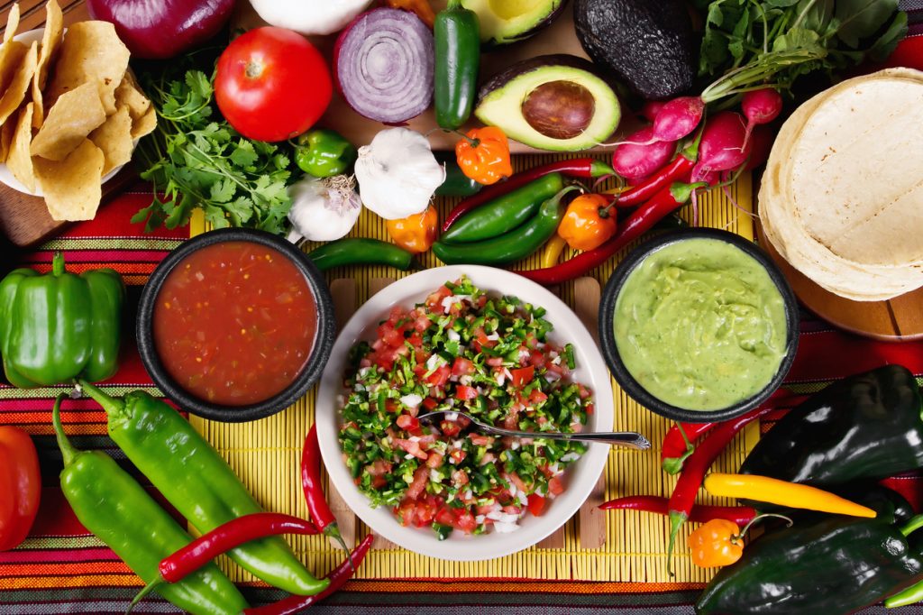 A table with pico de gallo, guacamole, and vegetables