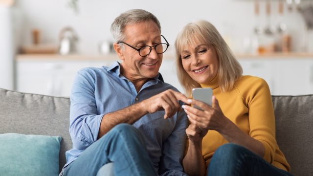 An older couple sitting on the couch looking at a cell phone together.