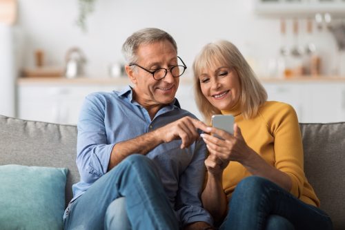 An older couple sitting on the couch looking at a cell phone together.