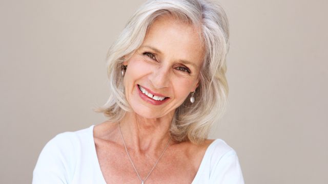 Close up portrait of beautiful older woman with blonde/gray hair smiling and standing by wall