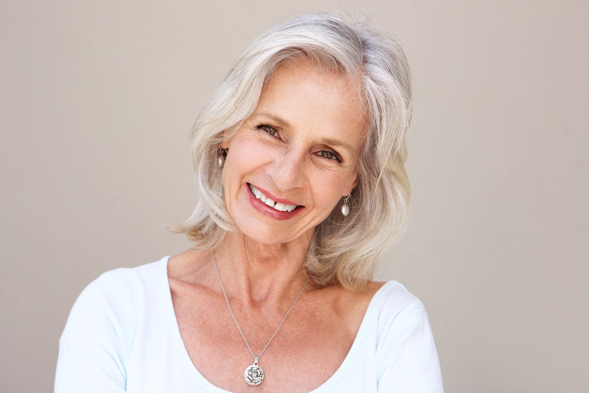 Close up portrait of beautiful older woman with blonde/gray hair smiling and standing by wall