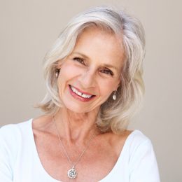 Close up portrait of beautiful older woman with blonde/gray hair smiling and standing by wall