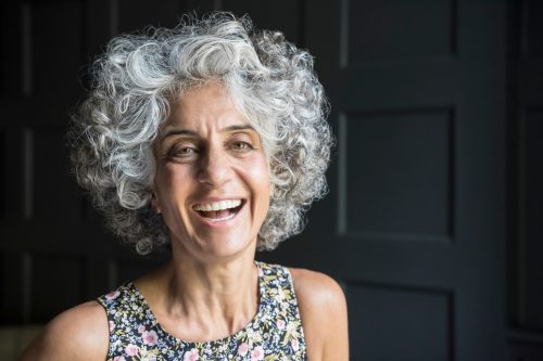 Portrait of a woman in her 50s with cheerful expression, with short curly gray hair.