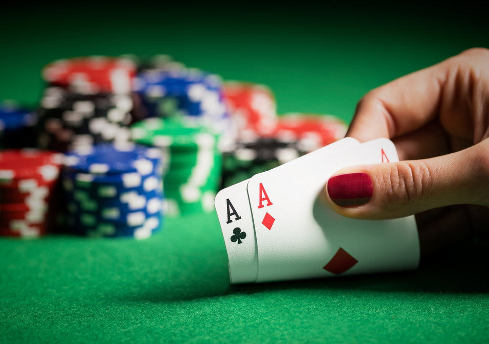 A close up of a hand looking at pocket aces on a poker table