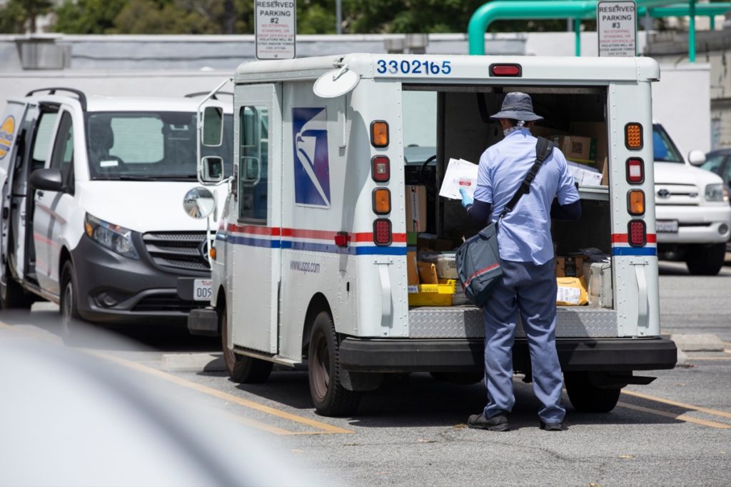 A mail truck and a USPS (United States Parcel Service) postal carrier make a delivery.