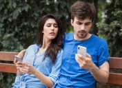 young couple sitting in the park with cell phones