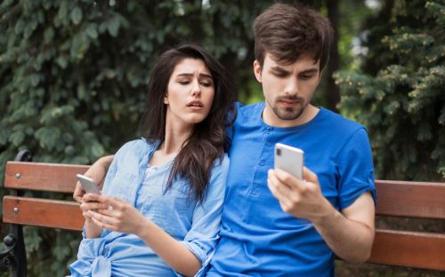 young couple sitting in the park with cell phones
