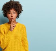 Young Black Woman Putting One Finger To Her Mouth