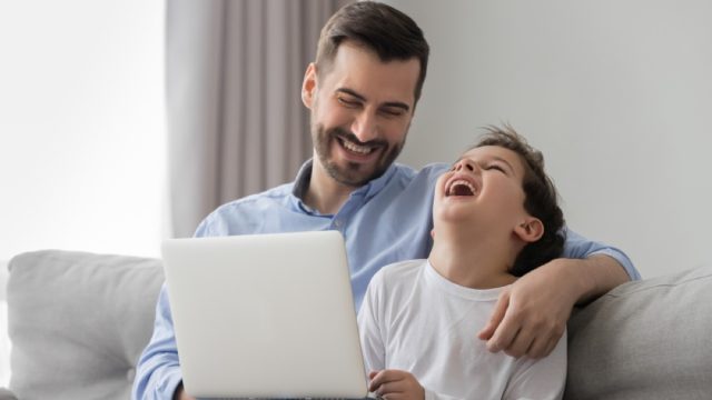 dad jokes - father and son looking at a computer screen and laughing on a couch