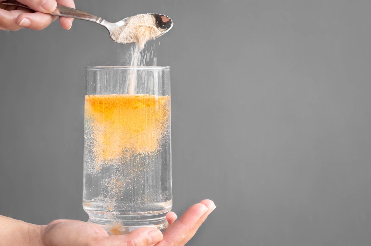 yellow Electrolyte Powder pouring into glass of water on gray background