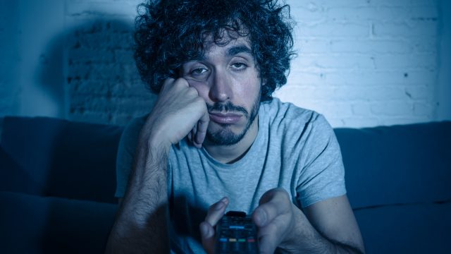 man looking bored sitting on couch holding remote - things to do when bored