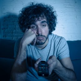man looking bored sitting on couch holding remote - things to do when bored