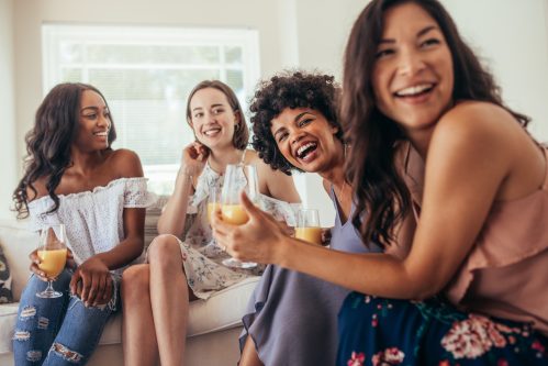 group of women laughing on couch with drinks 