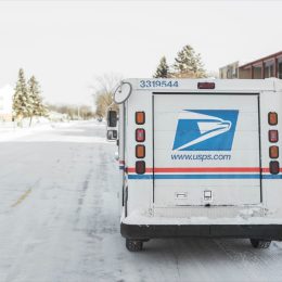 USPS, United States Postal Service, van parked on suburban street during winter with lots of snow.