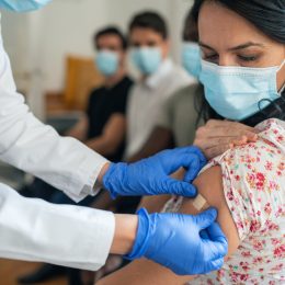 A doctor putting a bandage on a woman's arm who's wearing a mask after receiving a COVID booster shot