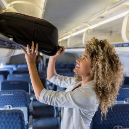 A young woman putting her carry-on luggage into an overhead bin