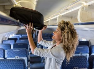 A young woman putting her carry-on luggage into an overhead bin