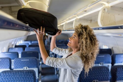 A young woman putting her carry-on luggage into an overhead bin