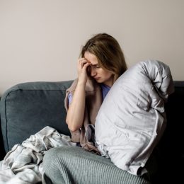 A young woman sitting on the couch with symptoms of long COVID