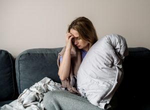 A young woman sitting on the couch with symptoms of long COVID