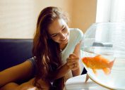 A woman looking at a goldfish in a bowl