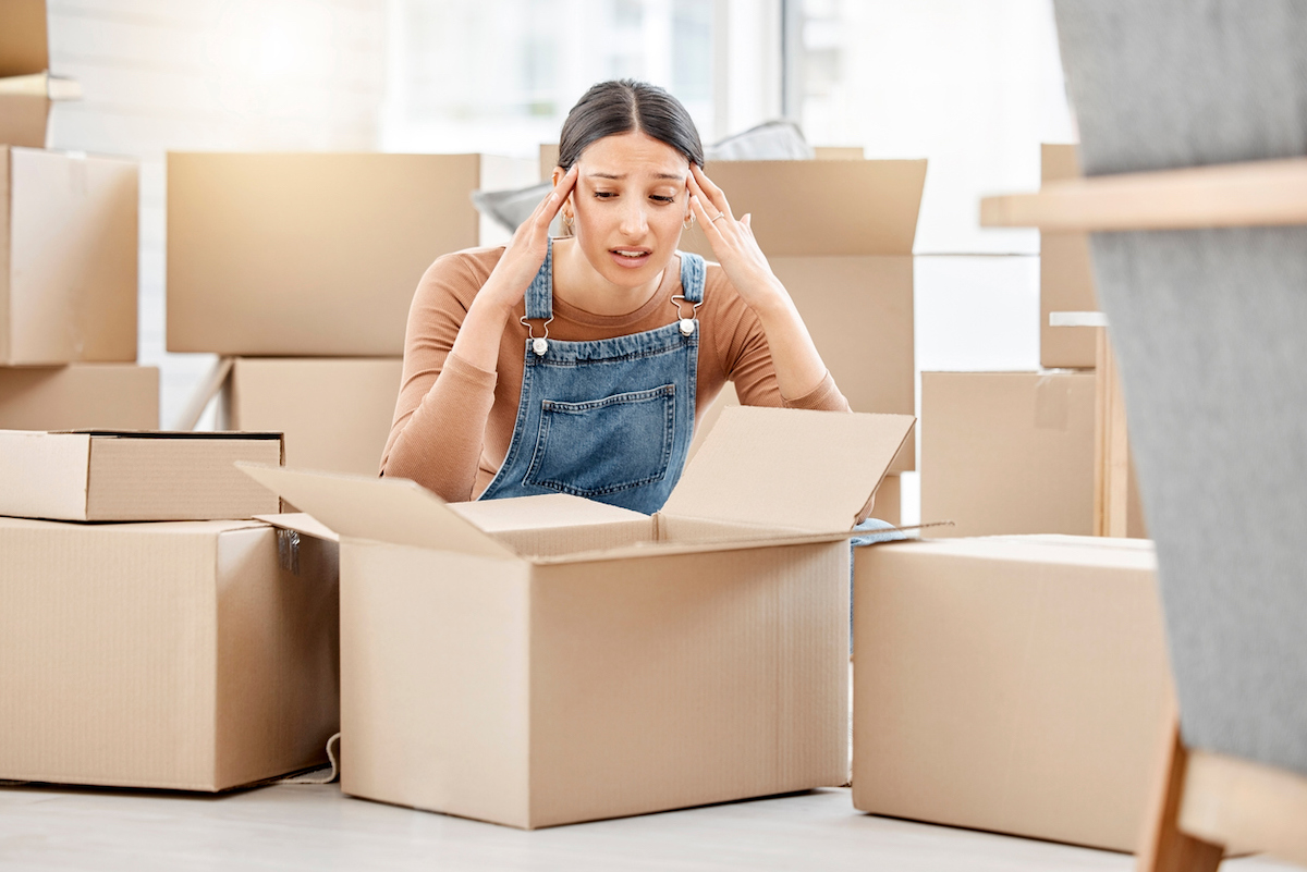 A young woman packing boxes to move and looking stressed.