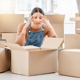 A young woman packing boxes to move and looking stressed.