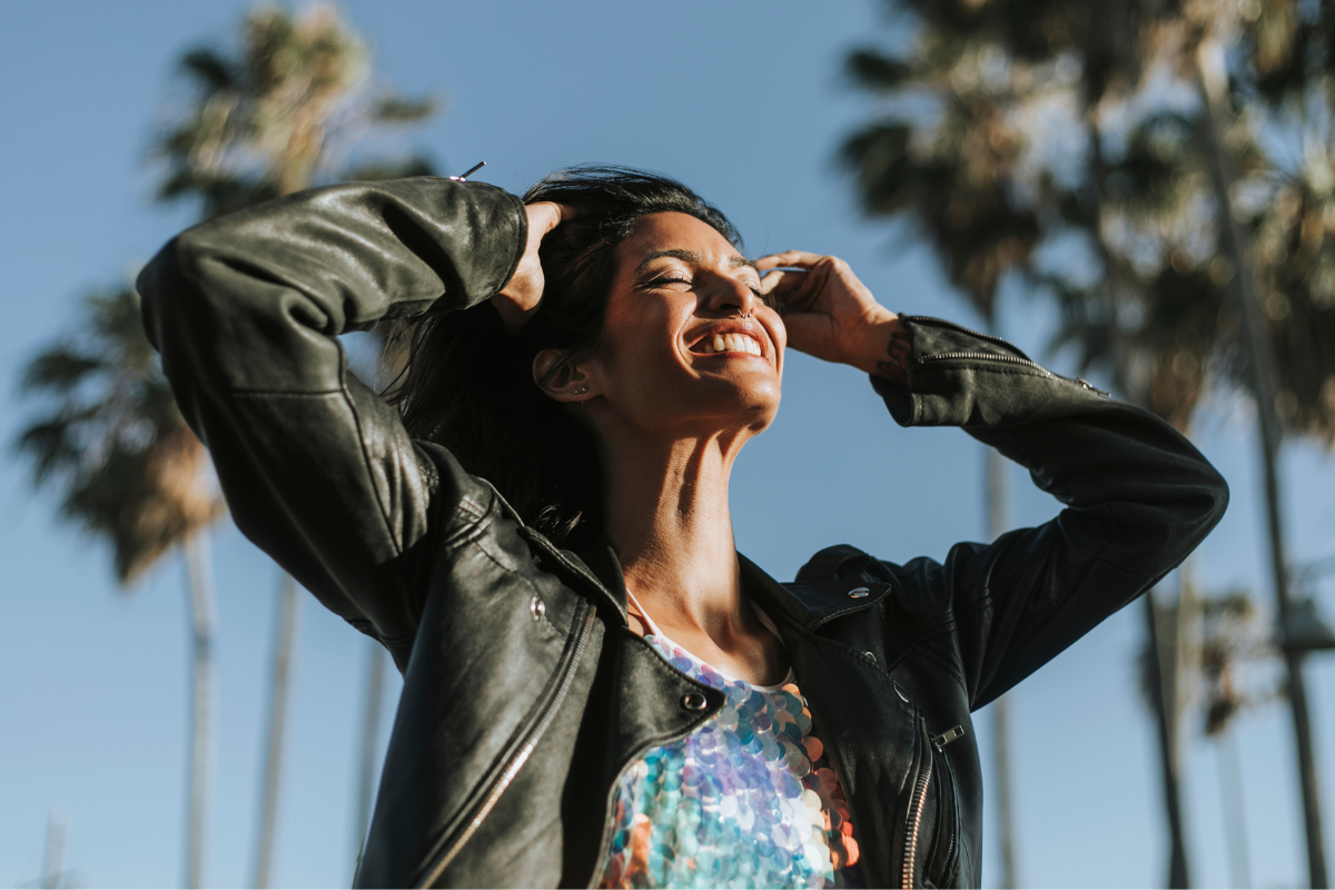 woman smiling in leather jacket near palm trees
