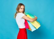 woman in a skirt on a blue background holding multicolored packages with a greedy look