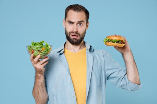 man holding a burger and a salad - would you rather questions about food