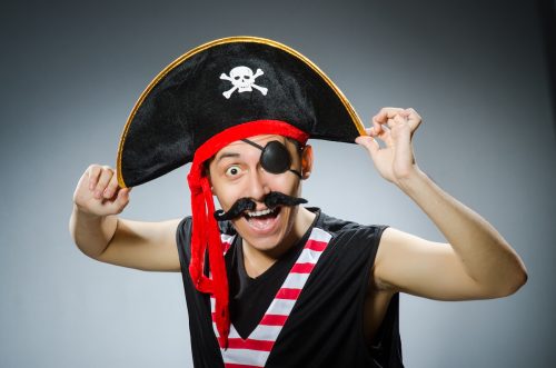 Young man dressed as a funny pirate against a gray background