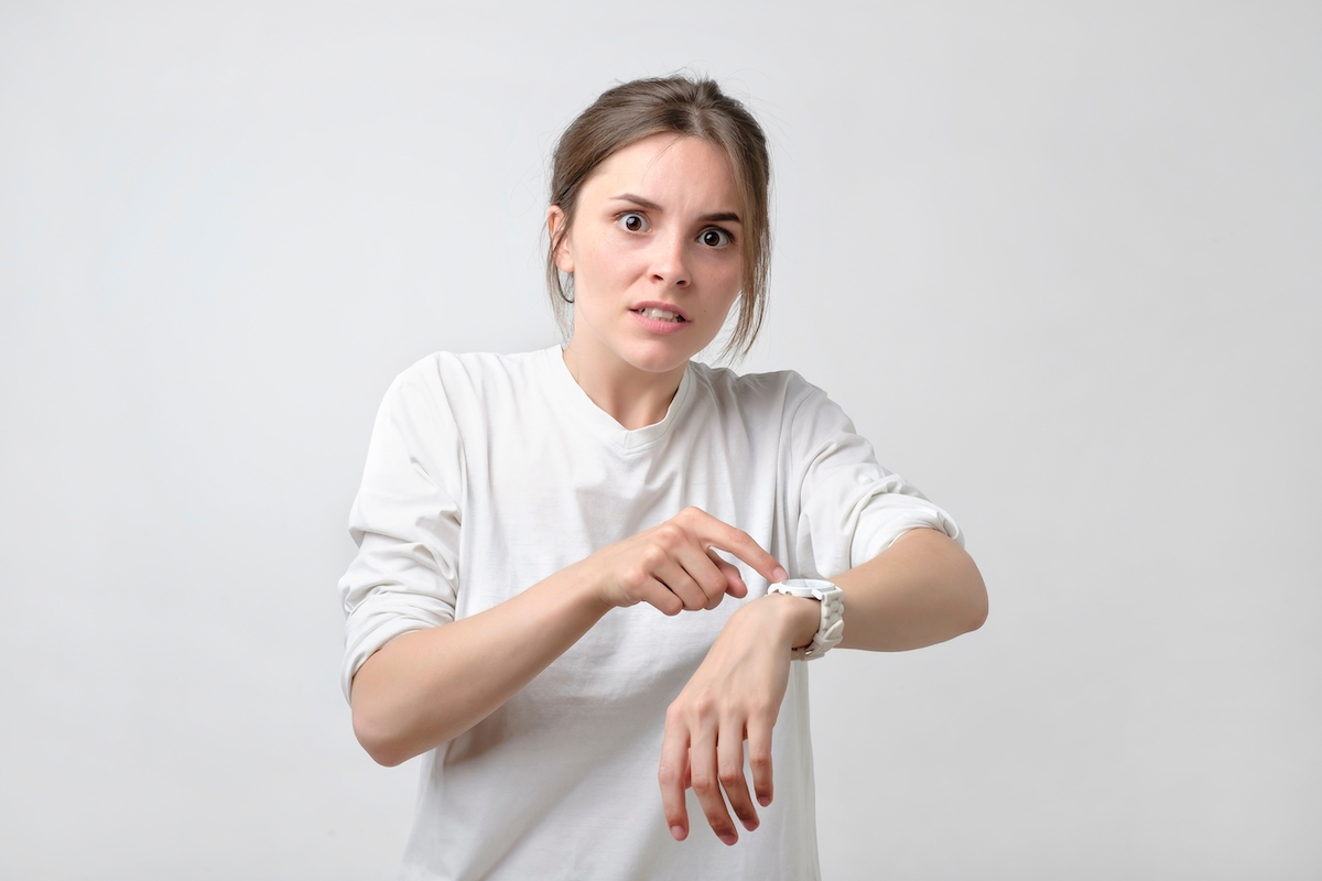 Young pretty caucasian student is angry because of being late. She is showing time on her watch.