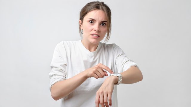 Young pretty caucasian student is angry because of being late. She is showing time on her watch.